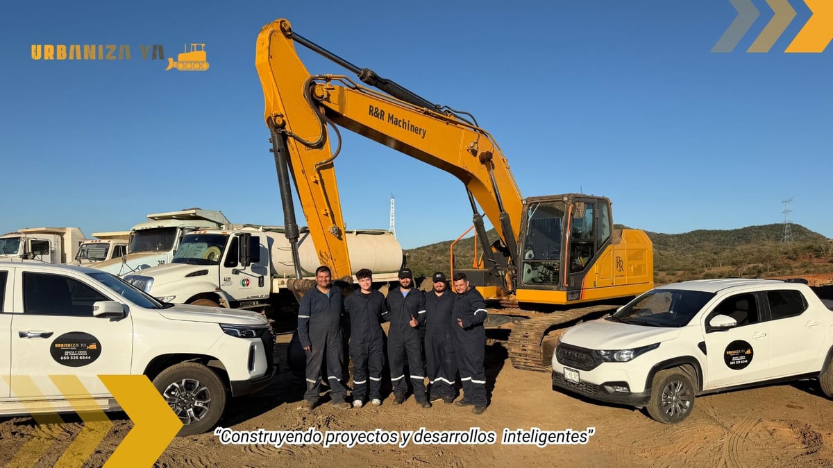 Group of people in business attire standing in front of a large yellow excavator with white vehicles on a desert landscape